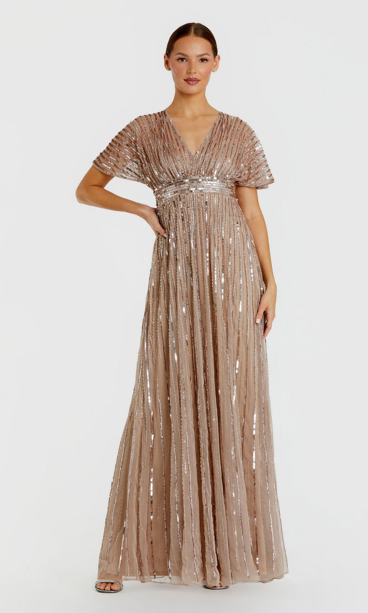 A woman poses against a plain white background wearing the Mac Duggal 94204 Long Formal Dress in taupe. This floor-length gown features short sleeves and vertical sequin stripes, with dazzling beaded details that create an effortlessly elegant look.